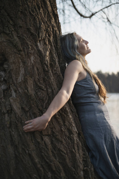 Close up woman spiritually connecting with willow tree portrait picture. Healing. Closeup side view photography with blurred background. High quality photo for ads, travel blog, magazine, article - Foto, imagen