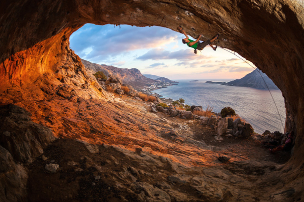 Muž horolezec stoupání podél střechy v jeskyni při západu slunce - Fotografie, Obrázek