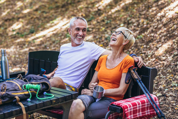 Mature couple sitting and drink coffee or tea while resting in the forest after hiking. - Photo, image
