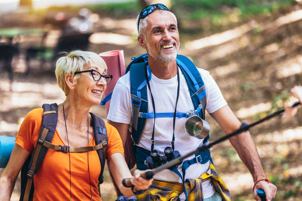 Mature couple hiking in forest wearing backpacks and hiking poles. Nordic walking, trekking. Healthy lifestyle. - Fotó, kép