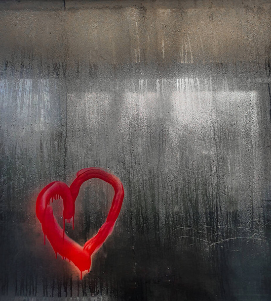 A red heart shape graffiti pictured on the wet protective plastic of a bus station creating a moody image with copy space. - Photo, Image