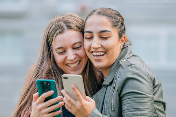 друзі з мобільними телефонами посміхаються обіймаючись на вулиці
 - Фото, зображення
