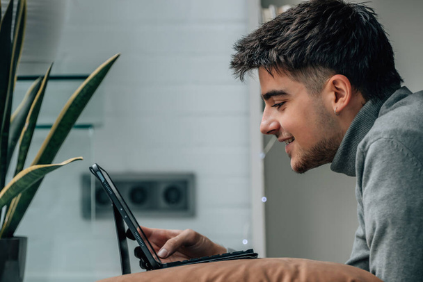 молодой человек смотрит на компьютер или ноутбук дома - Фото, изображение