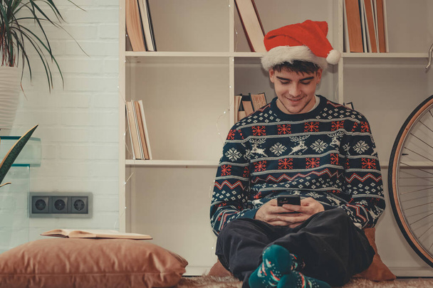 Genç adam ya da genç kız Noel 'de evde cep telefonuyla sohbet ediyor. - Fotoğraf, Görsel