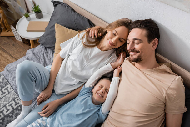 high angle view of happy family with closed eyes lying on bed  - Photo, image