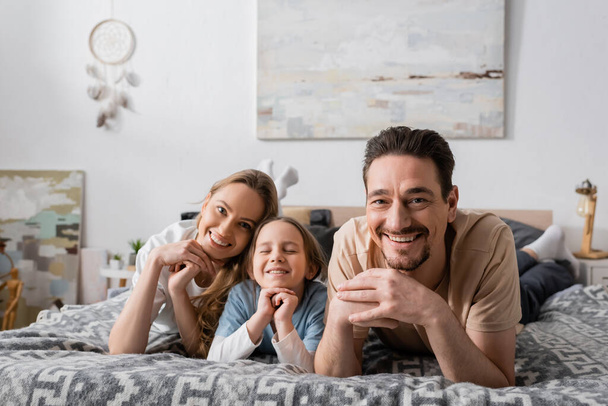portrait of joyful parents and kid looking at camera while resting in bedroom  - Valokuva, kuva