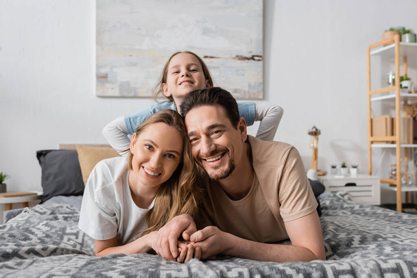 portrait of happy child behind positive parents looking at camera while resting in bedroom  - Foto, Bild