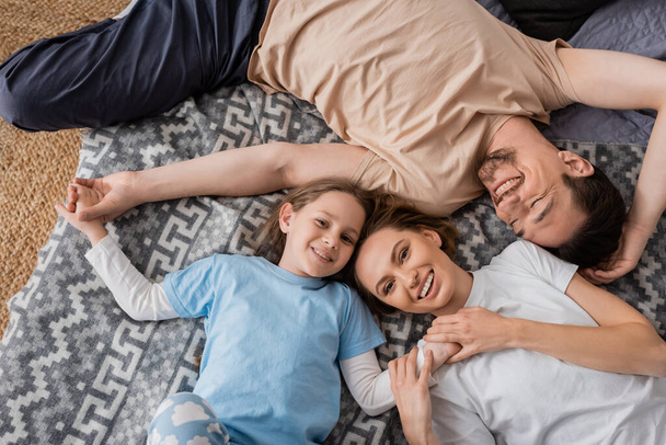 ylhäältä iloiset vanhemmat ja positiivinen tytär makaa sängyssä kotona   - Valokuva, kuva
