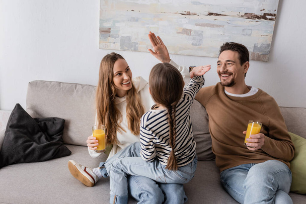 Ребенок дал пять веселой матери рядом с счастливым отцом, сидящим со стаканом апельсинового сока  - Фото, изображение