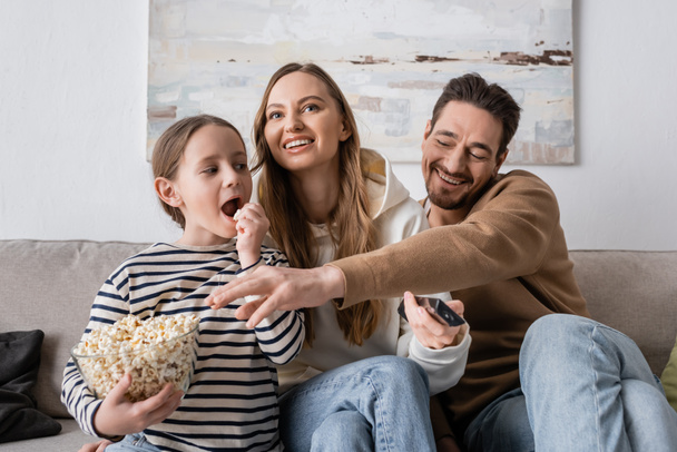 lapsi etsii onnellinen isä ottaen popcorn lähellä iloinen äiti kauko-ohjain   - Valokuva, kuva