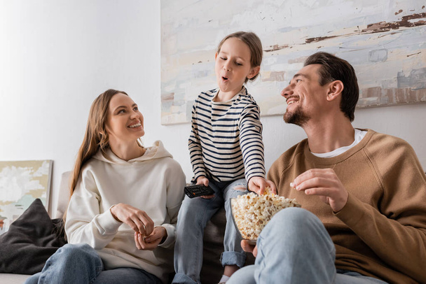 kid holding remote controller and reaching popcorn near happy parents  - Foto, immagini