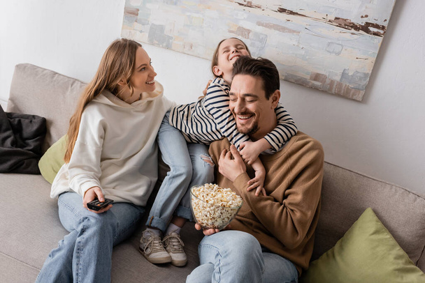 happy kid hugging bearded father with popcorn near smiling mother  - Fotografie, Obrázek