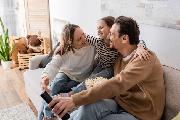 cheerful child hugging happy parents with popcorn and remote controller  - Foto, Bild
