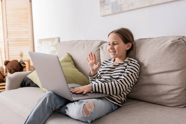 preteen girl in casual clothes having video call on laptop while sitting on couch  - Photo, Image