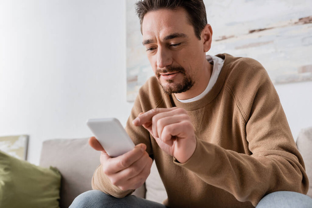 bearded man in beige jumper using smartphone at home  - Photo, image