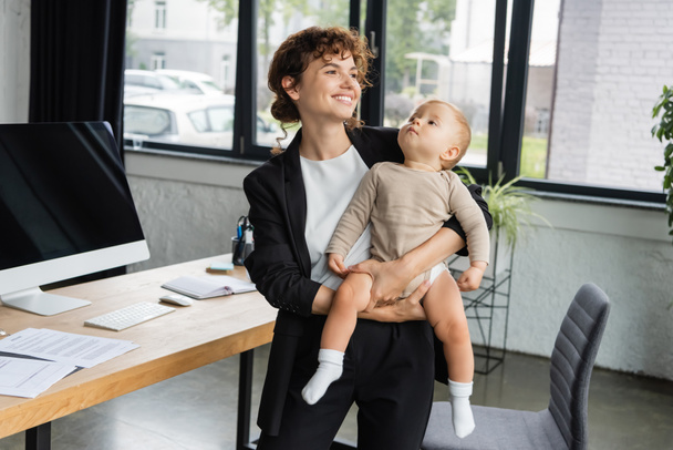 happy businesswoman looking away while standing with little child near computer monitor with blank screen - Foto, Imagem