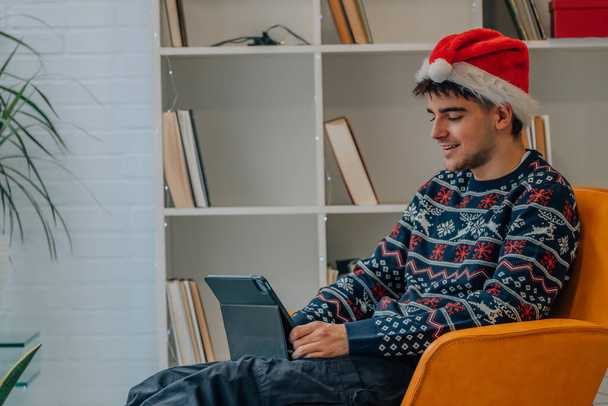 Nuori mies kotona jouluna kannettavan tietokoneen tai tabletin kanssa - Valokuva, kuva