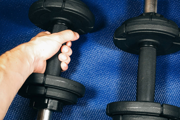 Man takes Heavy black dumbbells lying on the sports mat in the gym. Fitness sport motivation. Happy healthy lifestyle living. Exercises with bars weights. Home sport training. - Photo, Image
