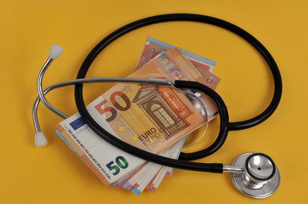 Stethoscope with a wad of euro banknote close-up on a yellow background  - Valokuva, kuva