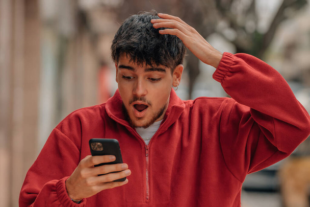 mladý muž s mobilním telefonem na ulici s překvapeným výrazem - Fotografie, Obrázek