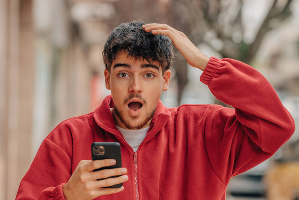 jeune homme avec téléphone portable dans la rue avec une expression surprise - Photo, image