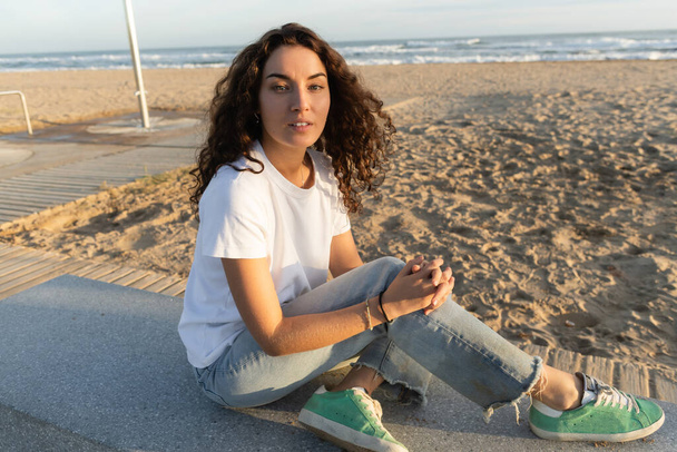 pretty woman with curly hair sitting on sandy beach near sea in Barcelona  - Fotografie, Obrázek
