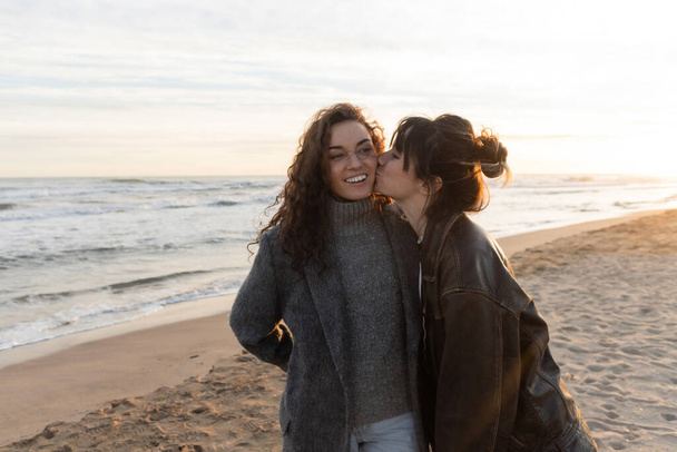 Молода жінка цілує щічку усміхненого друга на пляжі в Барселоні.  - Фото, зображення