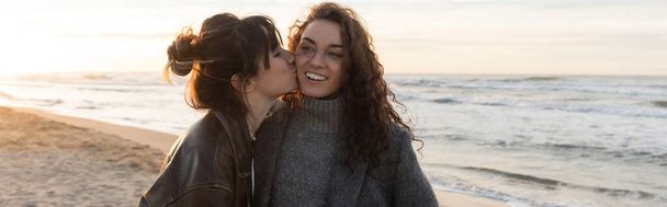 Young woman kissing cheeks of cheerful friend on beach in Spain, banner  - Photo, Image