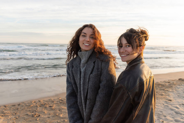İspanya 'nın kumlu sahilinde kameraya bakan neşeli genç kadınlar.  - Fotoğraf, Görsel