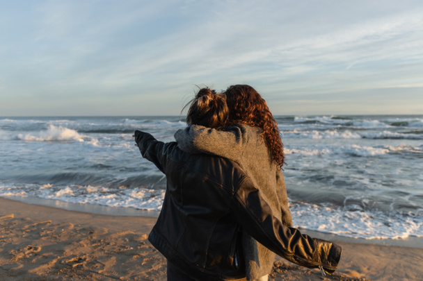 Back view of woman hugging friend on beach in Barcelona  - 写真・画像