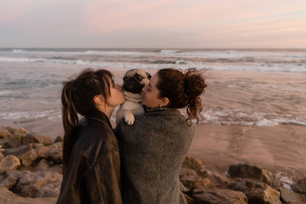 Friends kissing pug dog on beach in evening in Barcelona  - Photo, Image