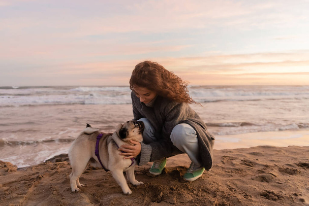 Curly woman petting pug dog on beach in Spain  - Foto, Imagem