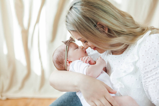 Baby girl and her beautiful young mother in a cozy house, light pastel colors. Newborn. Motherhood. - Foto, imagen