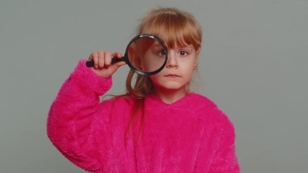 Curious investigator researcher scientist young preteen child girl kid holding magnifying glass near face looking in camera with big zoomed funny eye searching analysing. Nosy little toddler children - Felvétel, videó