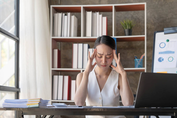 Les jeunes femmes asiatiques d'affaires sont stressées tout en travaillant sur un ordinateur portable, Femme d'affaires asiatique fatiguée avec des maux de tête au bureau, se sentant malade à l'espace de copie de travail dans un bureau à domicile... - Photo, image