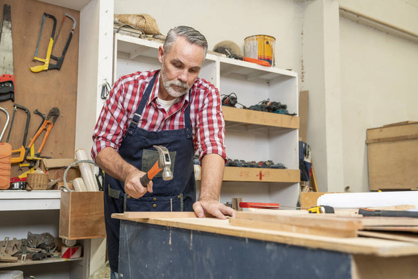 Male carpenter holding lumber, raw materials for furniture, measuring dimensions of cabinets for furniture in woodworking workshop at home - Photo, image