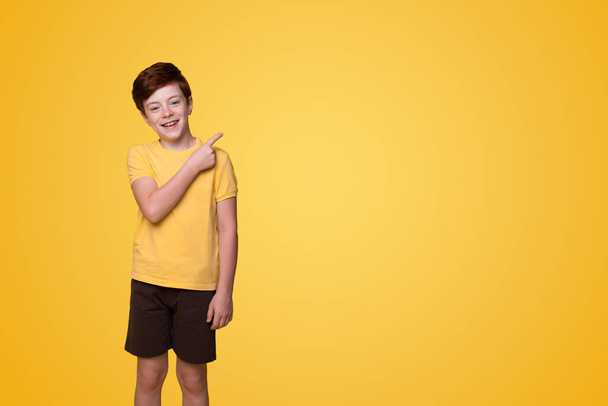 Little small happy boy pointing with his finger away at copyspace isolated over yellow background. Pointing up. Isolated portrait. - Photo, image