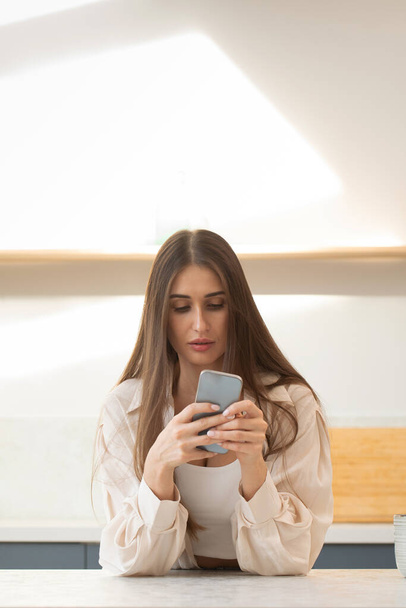 A young brunette woman uses her phone while making online purchases. Surfing the Internet, social networks. - Фото, изображение