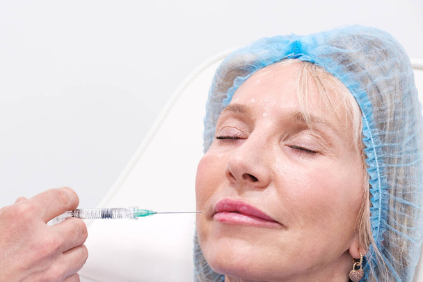Vertical picture of lips taking hyaluronic acid injections and Botox in an aesthetic clinic. Non-surgical treatment to reduce wrinkles and avoid aging. Copy space for titles and white background - Foto, Imagem