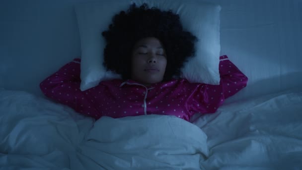 Top Άποψη της όμορφης νεαρής αφροαμερικάνας γυναίκας με αστείο αφρο χτένισμα κοιμάται άνετα σε άνετο κρεβάτι σε λευκά λινά και αγκαλιάζει μαξιλάρι υπνοδωμάτιο το βράδυ. Αργή κίνηση προσώπου με κλειστά μάτια - Πλάνα, βίντεο