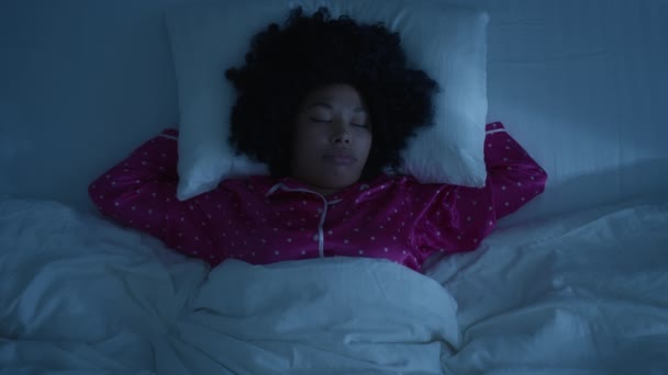 Slow motion face with closed eyes yawning. Beautiful young african american woman with funny afro hairstyle sleeping cozily in comfortable bed on white linens and hugging pillow bedroom at night 4K - Footage, Video