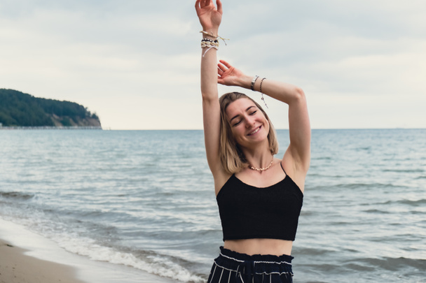 Young woman standing on blurred beachside background. Attractive female enjoying walking the sea shore. travel and active lifestyle concept. Springtime. Relaxation, youth, love, lifestyle solitude - Foto, imagen