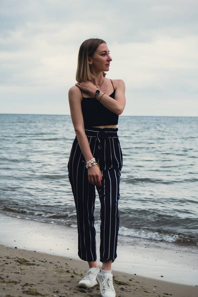 Young woman standing on blurred beachside background. Attractive female enjoying walking the sea shore. travel and active lifestyle concept. Springtime. Relaxation, youth, love, lifestyle solitude - Foto, Imagem