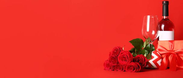 Μπουκάλι κρασί, ποτήρι, τριαντάφυλλο λουλούδια και δώρα σε κόκκινο φόντο με χώρο για κείμενο. Γιορτή του Αγίου Βαλεντίνου - Φωτογραφία, εικόνα