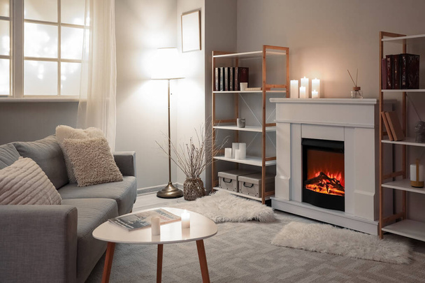 Interior of modern living room with fireplace, burning candles and shelving units - Photo, image