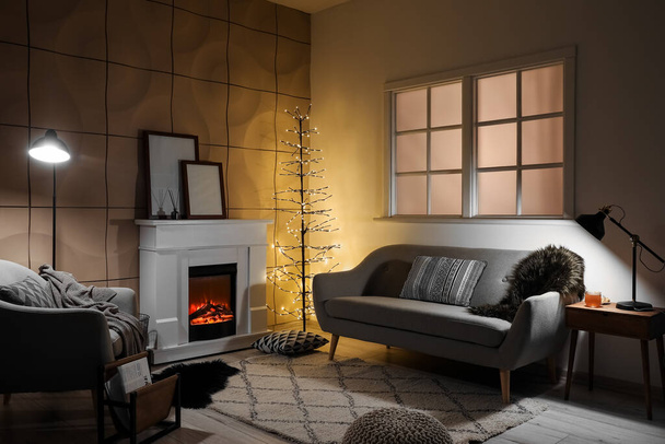 Interior of modern living room with electric fireplace, glowing lamps and sofa - Foto, immagini