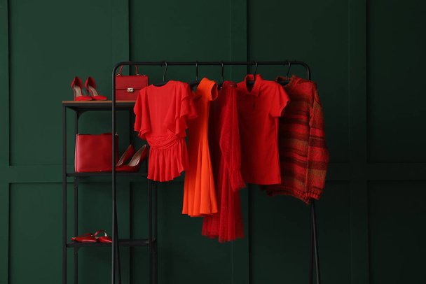 Rack with red female clothes, shelving unit and shoes near green wall - 写真・画像
