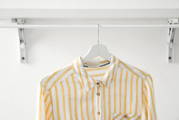 Striped shirt hanging on shelf near light wall, closeup - Fotó, kép