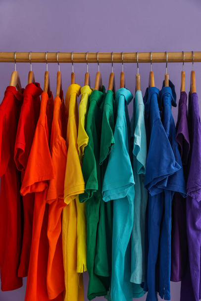 Стойка с красочными футболками возле сиреневой стены - Фото, изображение