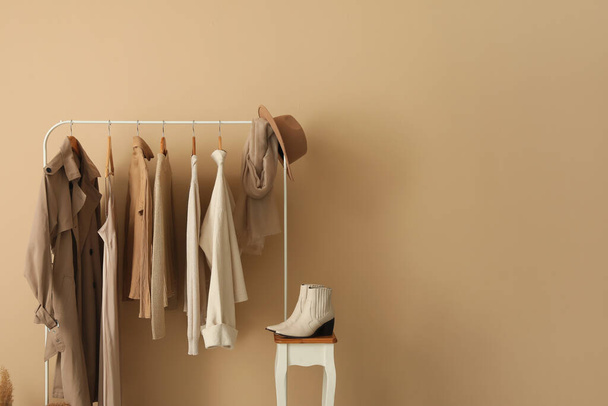 Rack with stylish clothes and shoes near beige wall - Zdjęcie, obraz